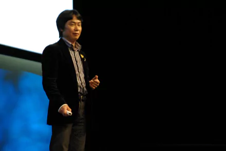 Shigeru Miyamoto presenting on stage, in a HD desktop wallpaper background.