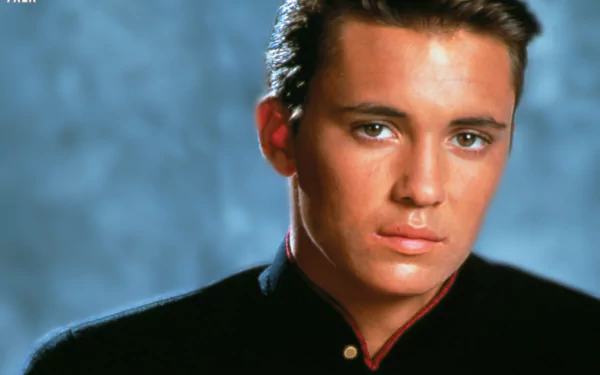 HD desktop wallpaper featuring a portrait of a young man with a dark shirt against a blue background.