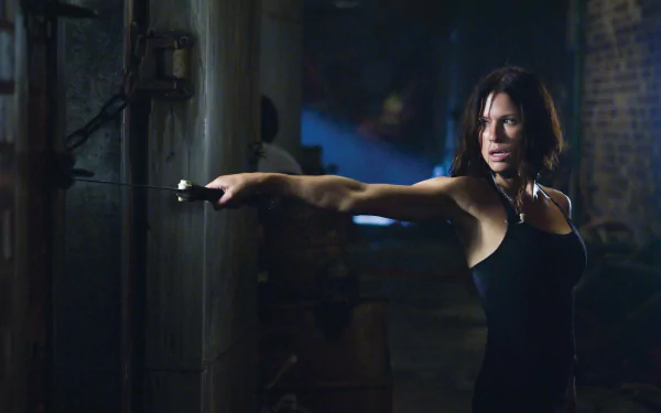 Movie Doomsday 2K Quad HD PC desktop wallpaper: tense woman in a black tank top brandishing a blade in a dim, industrial corridor, poised for action.