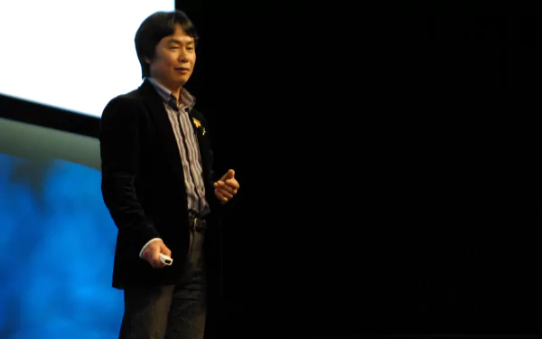 Shigeru Miyamoto presenting on stage, in a HD desktop wallpaper background.