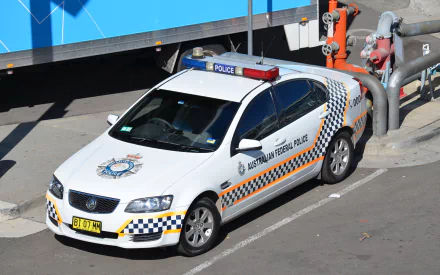 HD desktop wallpaper featuring a white Holden Omega police car with Australian Federal Police markings parked near industrial piping.