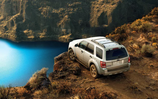 HD PC desktop wallpaper showcasing a silver Ford Escape vehicle parked on a rugged cliffside overlooking a vibrant blue lake.