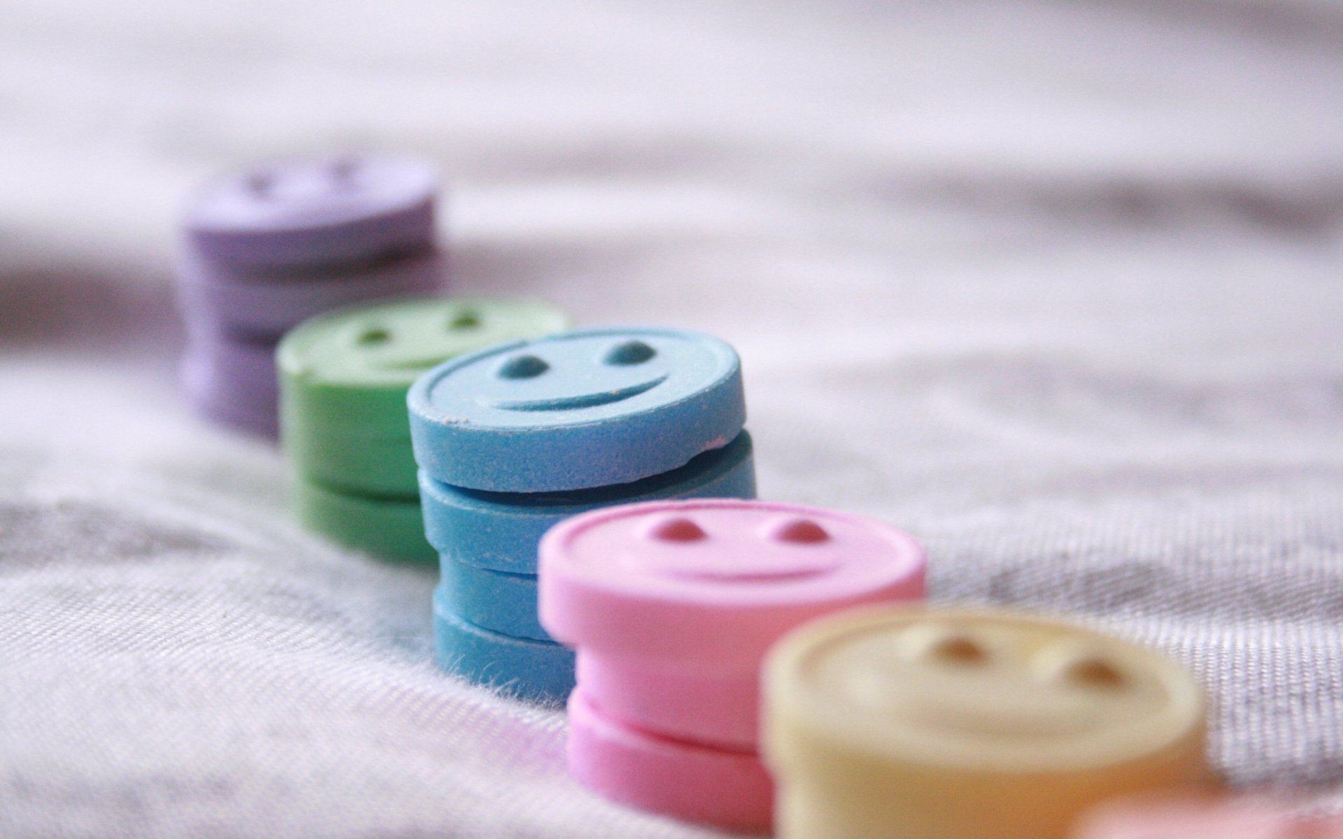 Colorful, round candy pieces with smiley faces arranged in a row, captured in a soft-focus close-up, presented as an HD PC desktop wallpaper and background.