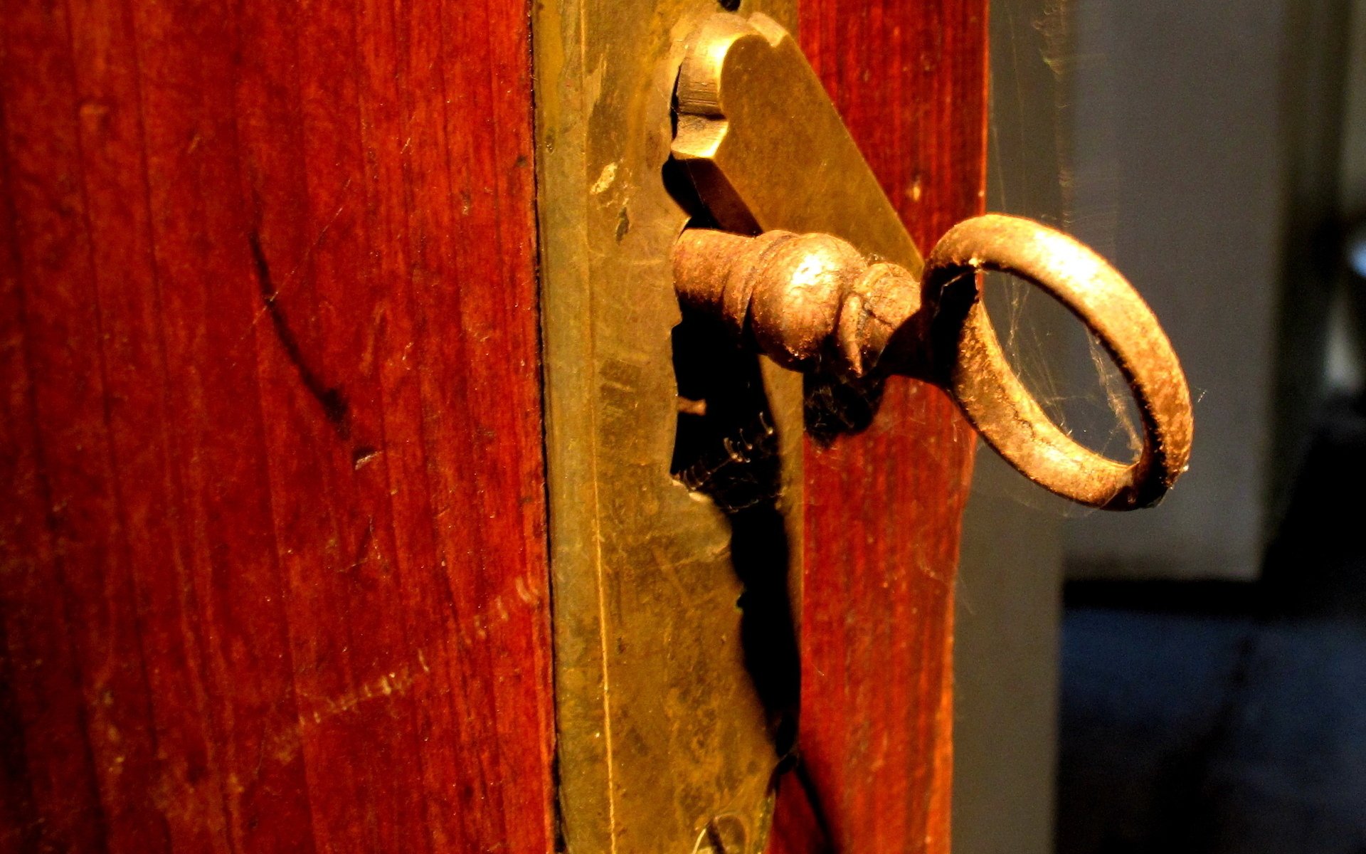 HD PC desktop wallpaper showing a close-up of an old, man-made brass key inserted in a wooden door lock, highlighting rustic textures and warm lighting.