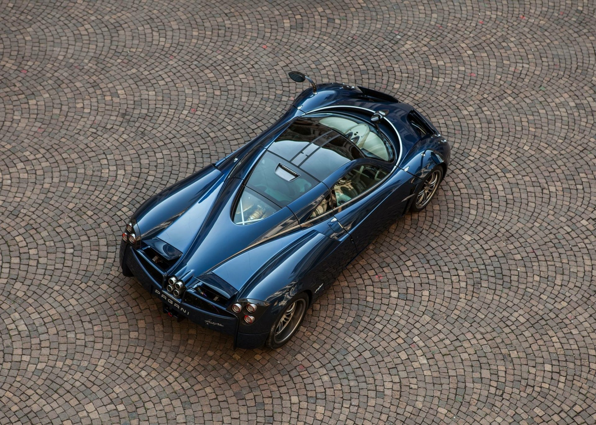 HD PC desktop wallpaper featuring a sleek, black Pagani vehicle captured from an elevated angle on a cobblestone surface.