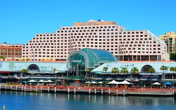 Novotel Sydney at Darling Harbour, Australia — stepped hotel building with a glass atrium on the waterfront under a clear blue sky, HD desktop wallpaper.