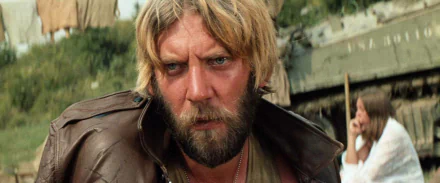 Movie still (Kelly's Heroes): intense bearded man in a worn leather jacket against a gritty outdoor wartime backdrop — HD PC desktop wallpaper/background
