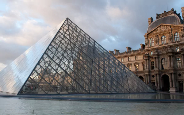 A stunning view of The Louvre in Paris, featuring the iconic glass pyramid against a dramatic sky, showcasing the blend of modern architecture with historic elegance.