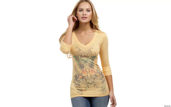 A woman, Elisandra Tomacheski, stands confidently in an HD desktop wallpaper. She is wearing a yellow, graphic-print, V-neck top with three-quarter sleeves and blue jeans against a white background.