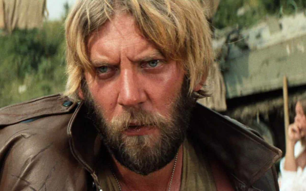 Movie still (Kelly's Heroes): intense bearded man in a worn leather jacket against a gritty outdoor wartime backdrop — HD PC desktop wallpaper/background