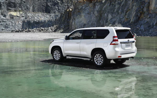 2014 Toyota Land Cruiser parked on a shallow, clear greenish water surface with rocky cliffs in the background, displayed as a HD PC desktop wallpaper.
