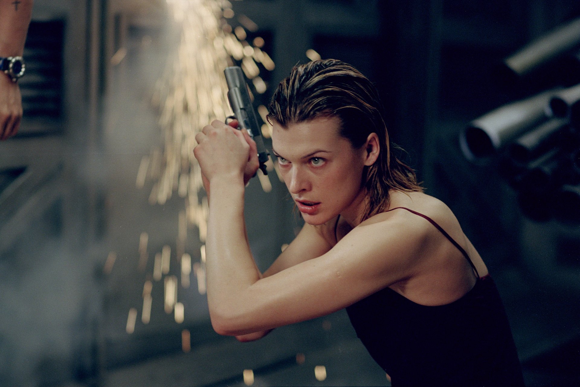 Milla Jovovich in an action-packed moment from the movie Resident Evil, showcasing intense energy with a gun, set against a backdrop of dynamic sparks and dark surroundings.