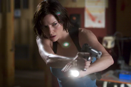 2K Quad HD desktop wallpaper: tense still from Resident Evil: Apocalypse — a female protagonist aims a handgun with a flashlight in a dim, cluttered interior.