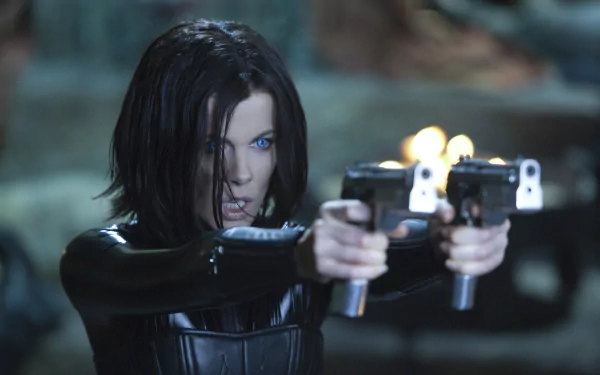 HD PC desktop wallpaper featuring a scene from the movie Underworld: Awakening, showing a fierce woman with glowing blue eyes aiming dual pistols.