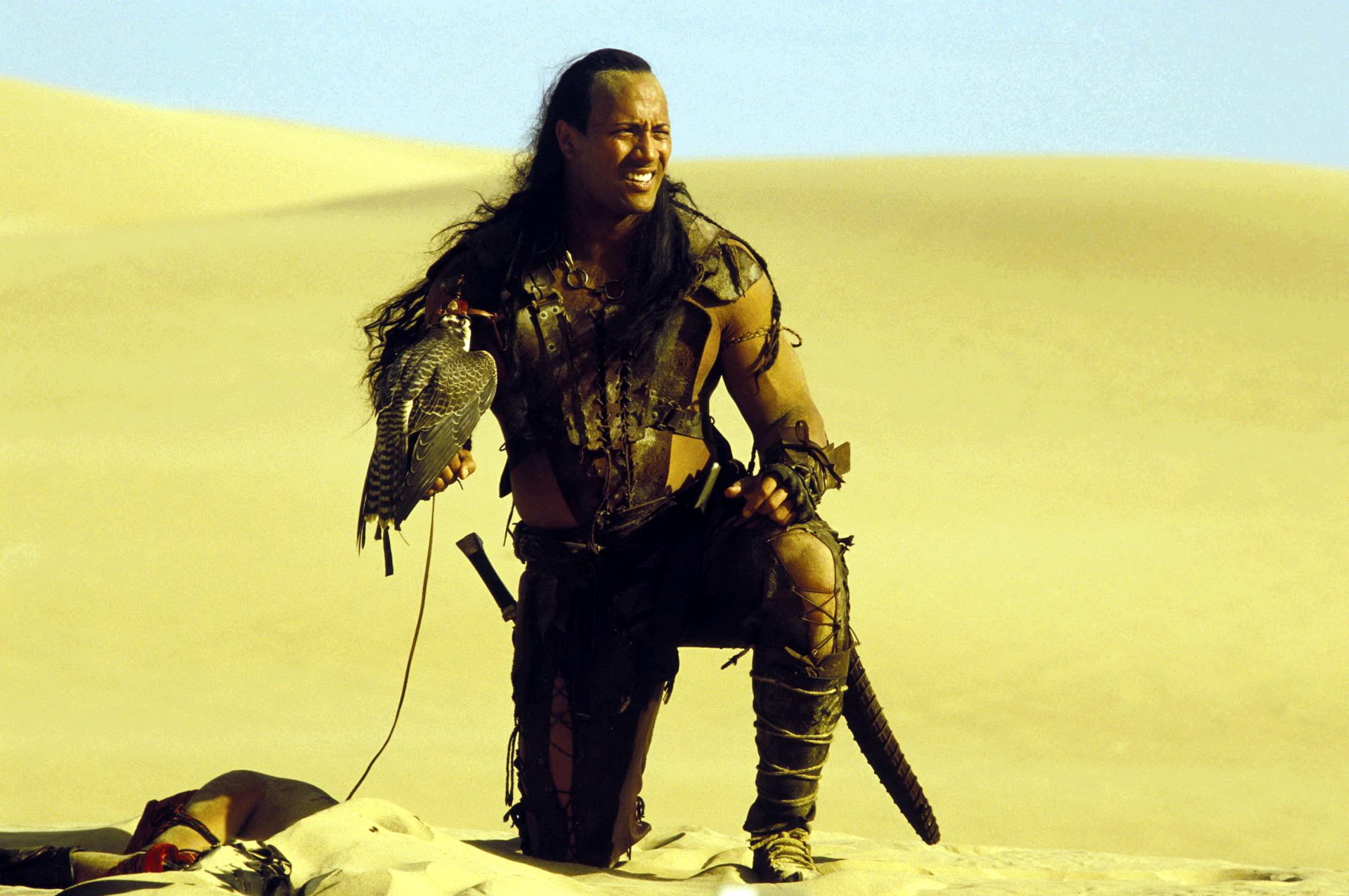 Armored warrior kneels on sunlit desert dunes clutching a hawk and scimitar — cinematic still from The Scorpion King, 2K Quad HD PC desktop wallpaper