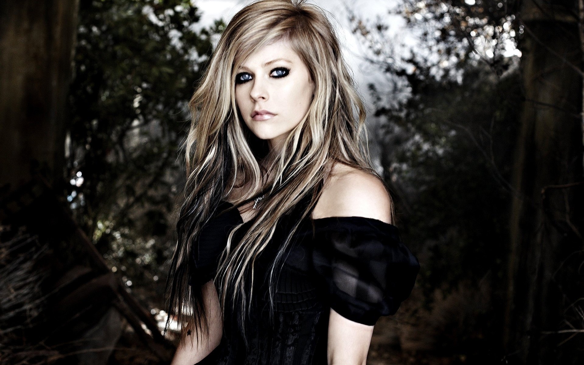 Avril Lavigne poses confidently in a dark, enchanting setting, showcasing her signature style. This HD wallpaper captures her unique artistry in music.