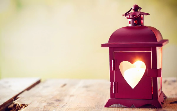 A red man-made lantern with a heart-shaped cutout, softly glowing on a rustic wooden surface, shown in an HD PC desktop wallpaper and background.