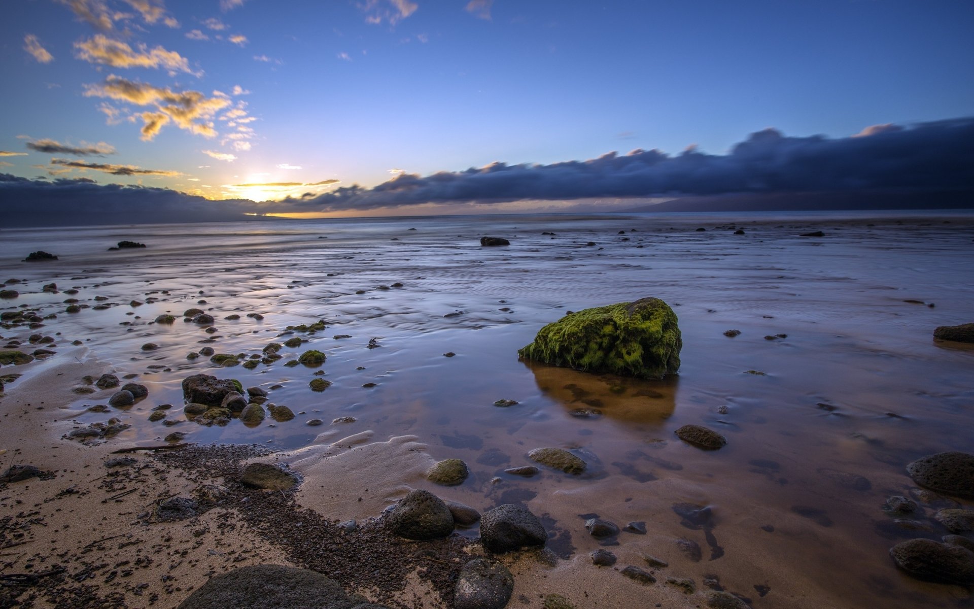 HD PC desktop wallpaper capturing a serene beach scene at low tide with scattered rocks and a vibrant sunset sky in the background.