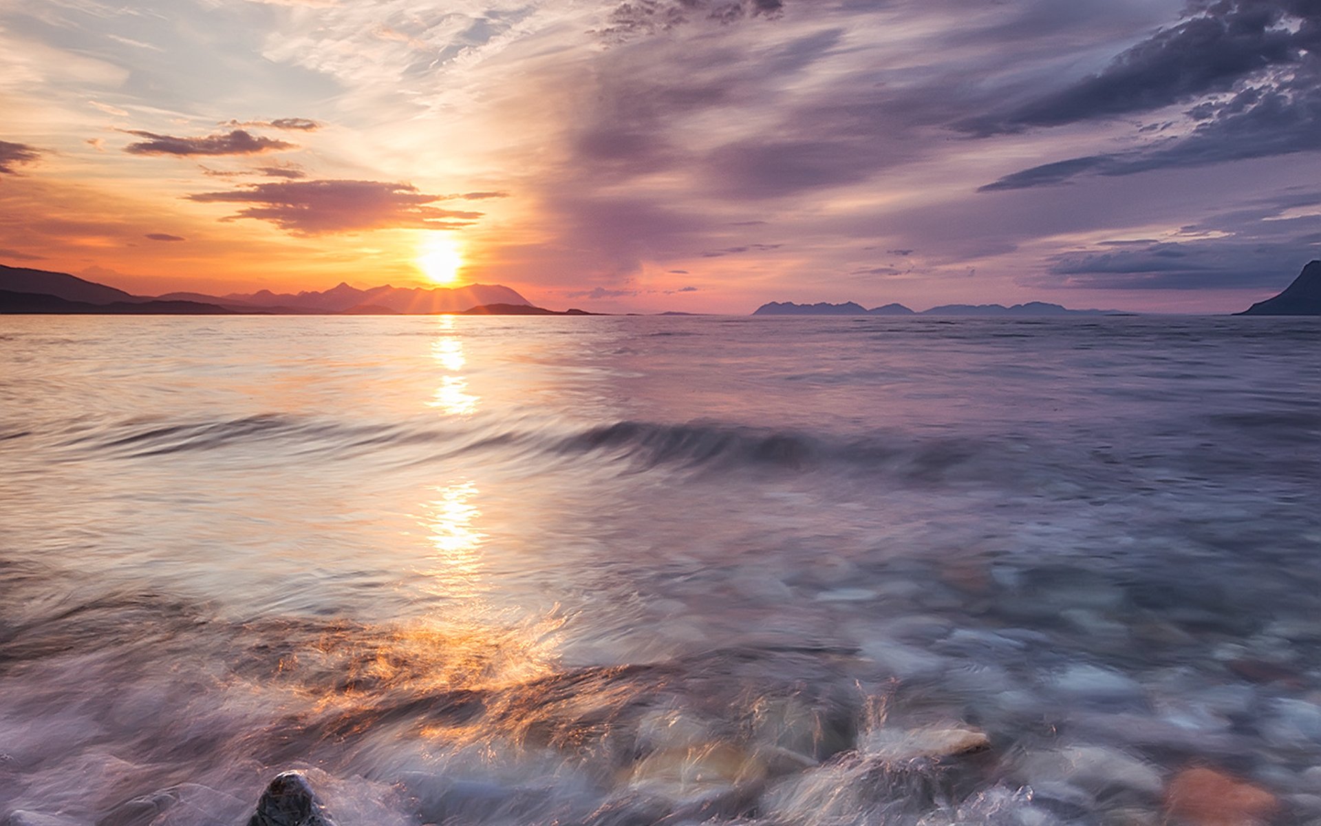 A stunning HD desktop wallpaper showcasing a vibrant sunset over calm waters, with gentle waves reflecting the hues of nature and a serene landscape in the background.