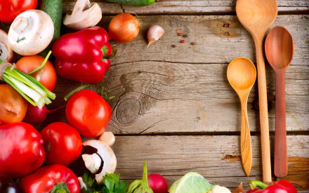 A vibrant display of fresh vegetables, including bell peppers, mushrooms, and herbs, arranged on a rustic wooden table alongside wooden spoons, creating a colorful food-themed desktop wallpaper.