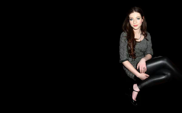 HD PC desktop wallpaper featuring celebrity Michelle Trachtenberg seated against a black background, wearing a gray top and black leather pants.
