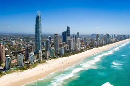 A stunning cityscape of Surfers Paradise, Gold Coast, Queensland, featuring towering skyscrapers alongside a pristine beach and vibrant ocean waves under a clear blue sky.