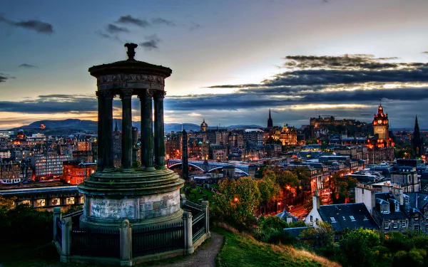 A stunning view of Edinburgh, Scotland, featuring a monument overlooking the city skyline at dusk, with vibrant lights illuminating the historic architecture.