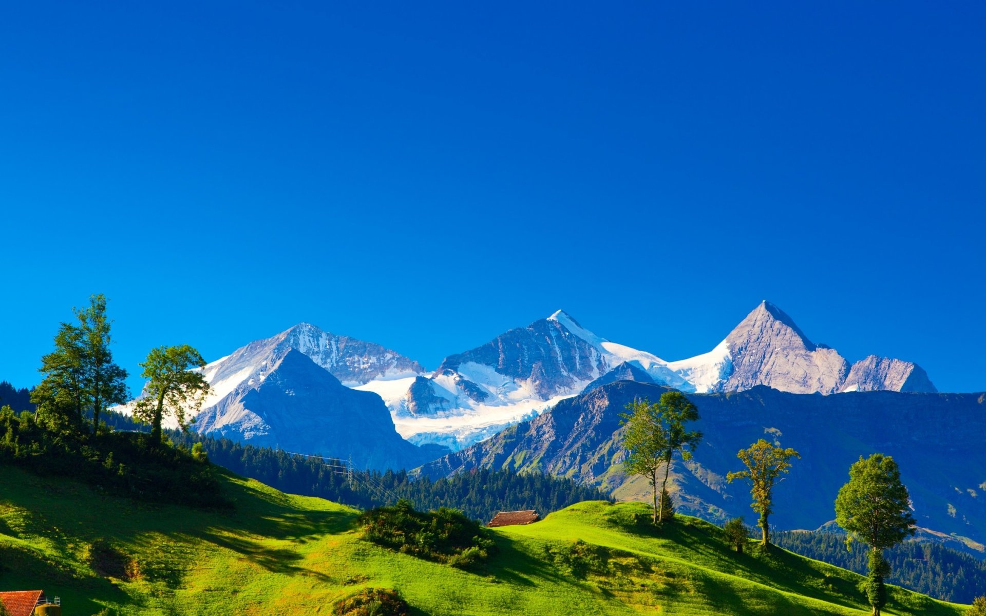 HD PC desktop wallpaper showcasing a vibrant mountain landscape with snow-capped peaks, lush green hills, and a clear blue sky in a stunning nature scene.