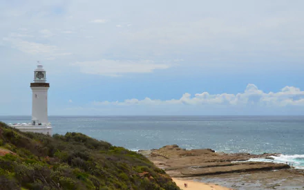 Norah Head Lighthouse stands on the rocky coastline by the beach, overlooking the ocean and horizon in Australia.