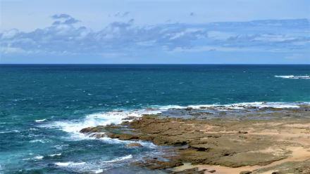 Norah Head coastline, Australia — ocean waves breaking over a rocky shore beneath a wide horizon; vibrant water and sky, HD desktop wallpaper.