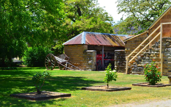 HD desktop wallpaper of Eskbank House in Lithgow, Australia, featuring a stone building, old cart, and lush green trees under a clear sky.