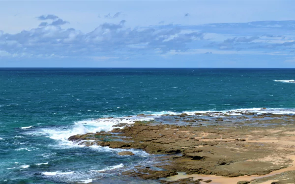 Norah Head coastline, Australia — ocean waves breaking over a rocky shore beneath a wide horizon; vibrant water and sky, HD desktop wallpaper.