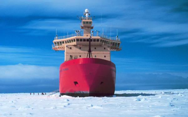 HD PC desktop wallpaper: red icebreaker ship vehicle breaking through Arctic sea ice, frontal view under a vivid blue sky over a frozen white expanse.