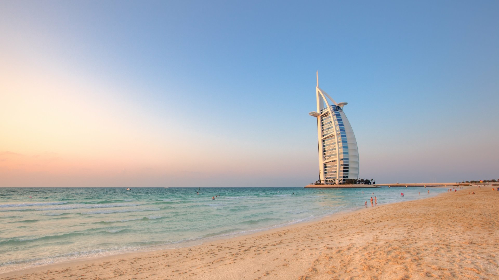4K Ultra HD wallpaper showcasing the man-made Burj Al Arab against a clear sky, with the serene beach and calm sea in the foreground.