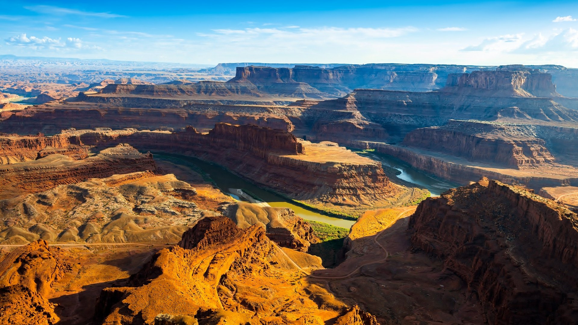 Vivid 4K Ultra HD desktop wallpaper showcasing a vast canyon landscape under a bright blue sky, highlighting dramatic rock formations and winding river below.