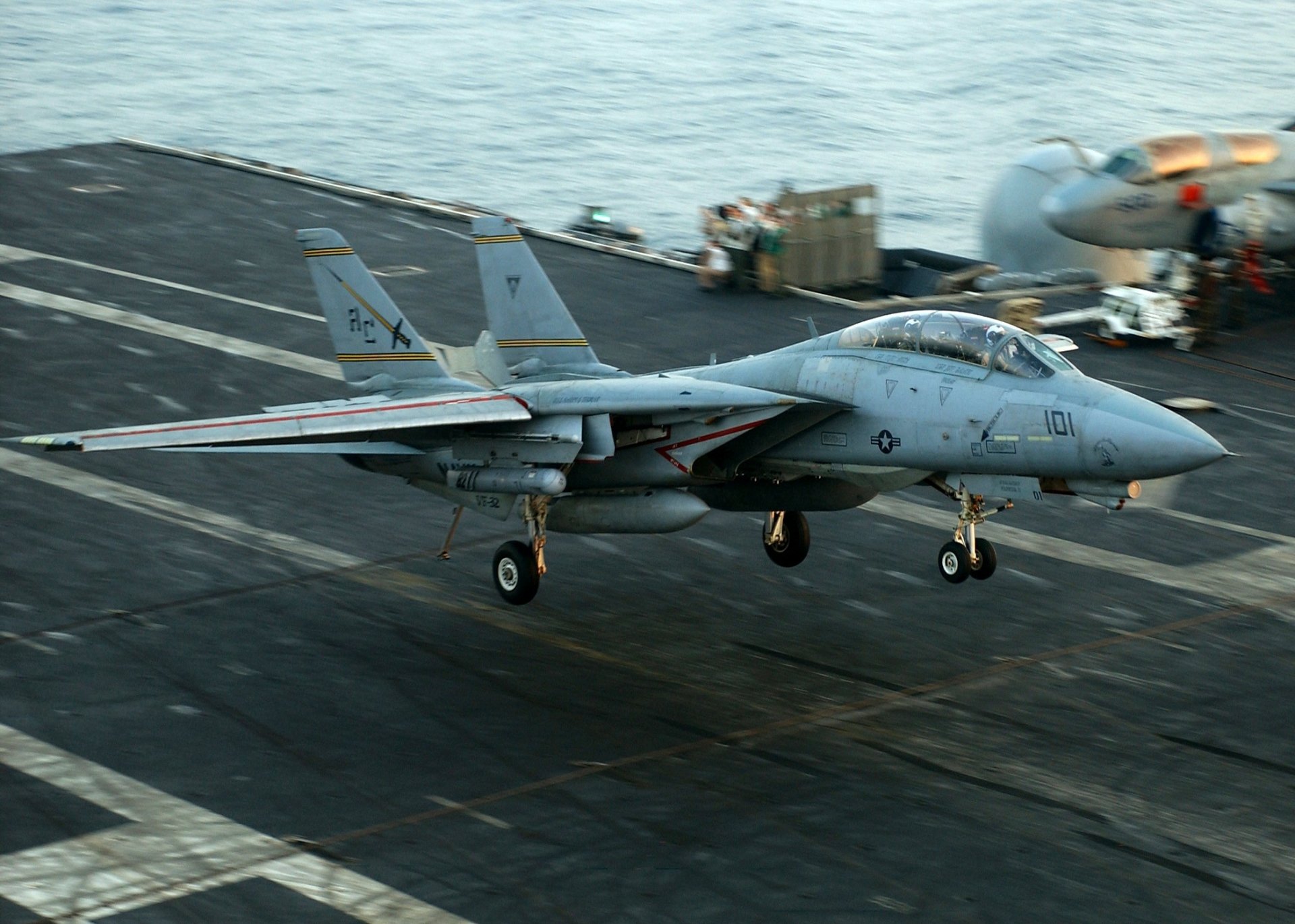 HD desktop wallpaper featuring a Grumman F-14 Tomcat military jet landing on an aircraft carrier deck over the ocean.
