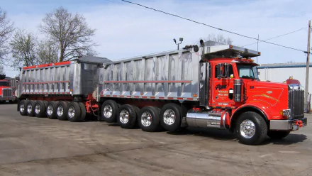 HD PC desktop wallpaper featuring a red Peterbilt dump truck with dual trailers parked on a paved lot under a clear sky.
