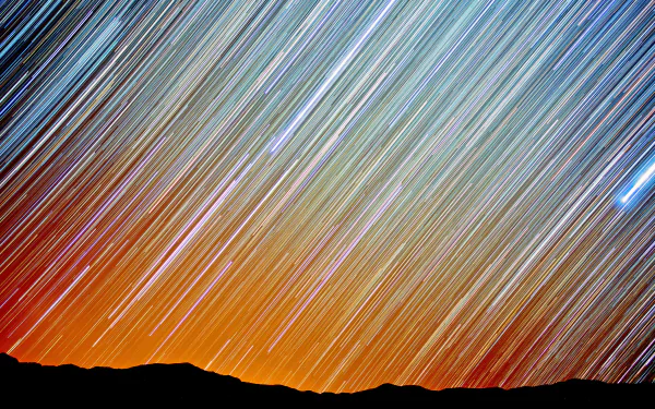 4K Ultra HD nature and sky wallpaper showing vibrant star trails streaking across the night sky above a silhouetted horizon.