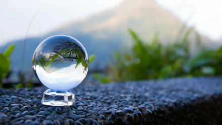 A glass globe sits on a textured surface, reflecting a serene landscape with greenery and mountains in the background. This high-definition image serves as an elegant desktop wallpaper.
