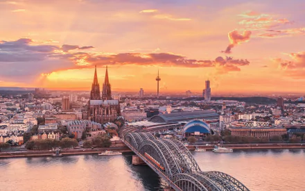 A vibrant night view of Cologne featuring the iconic cathedral, Hohenzollern Bridge, and city skyline, captured in HD as a man-made urban landscape.