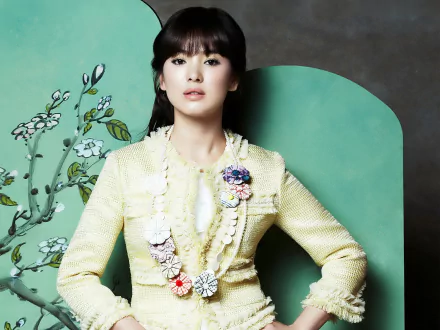 A stylish HD wallpaper featuring Korean actress Song Hye Kyo, showcasing her elegant outfit and poised expression against a vibrant green backdrop with floral accents.