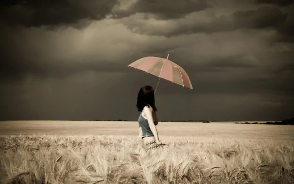HD wallpaper of a woman in a field holding an umbrella under a moody, overcast sky.