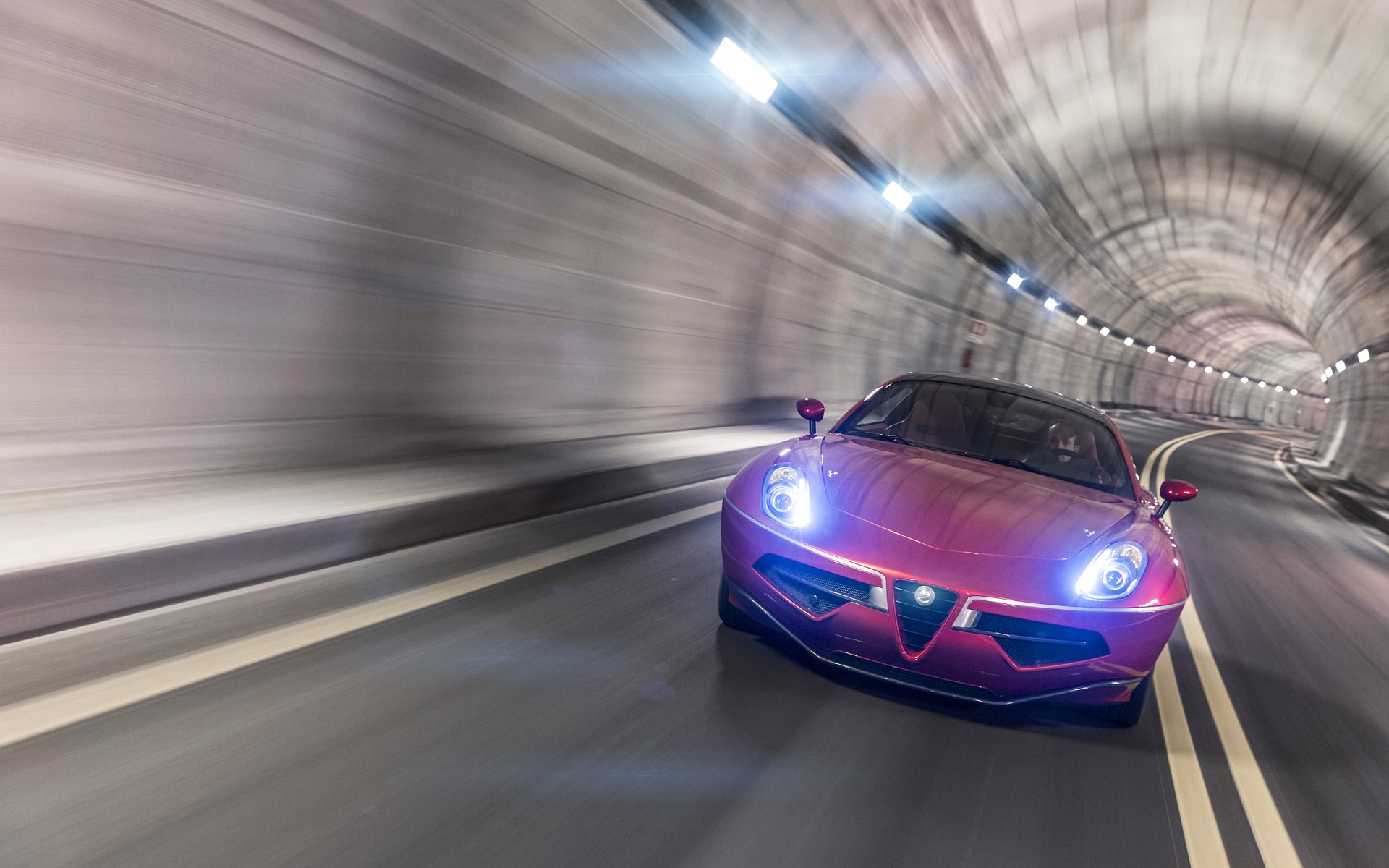 Red Alfa Romeo Disco Volante vehicle racing through a lit tunnel, motion-blurred 2K Quad HD PC desktop wallpaper background showcasing the car's front profile and headlights.