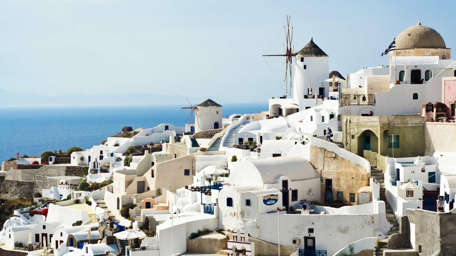 4K Ultra HD image of Santorini’s iconic whitewashed buildings and windmills set against a clear blue sky and sea, showcasing stunning man-made architecture.