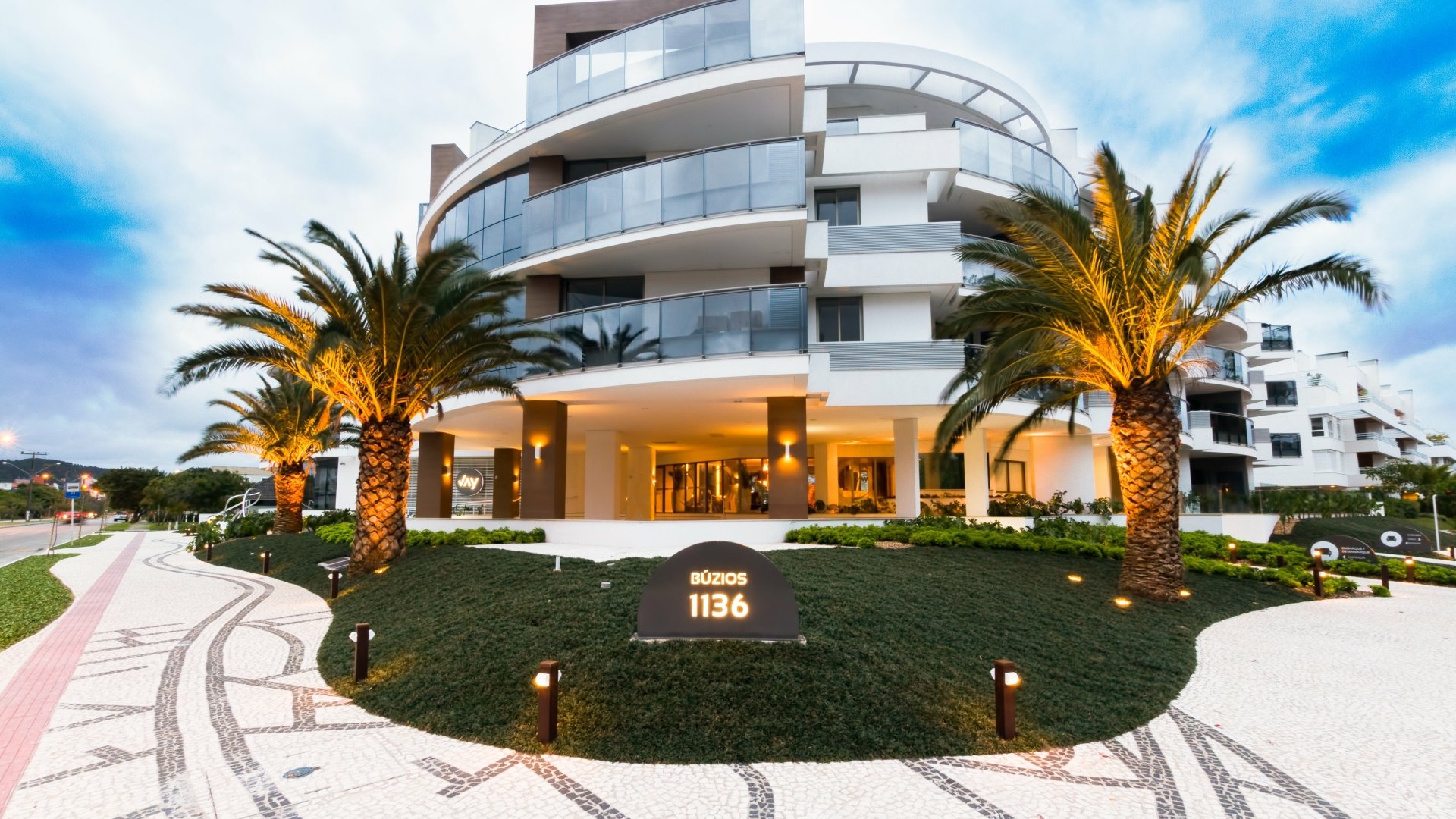 4K Ultra HD desktop wallpaper featuring a modern man-made building with curved balconies, illuminated palm trees, and a well-lit entrance.