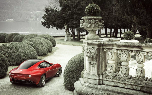 Red Alfa Romeo Disco Volante vehicle parked on an ornate lakeside terrace with topiary and stone balustrade — 2K Quad HD PC desktop wallpaper/background.