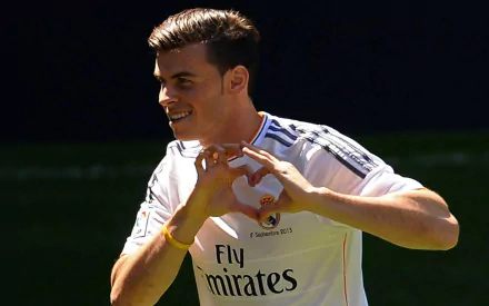 Gareth Bale in Real Madrid C.F. white jersey, smiling and forming a heart with his hands during a sports event, captured in a HD desktop wallpaper image.