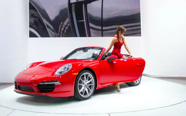 A sleek red Porsche convertible showcased indoors with a woman in a red dress stepping out, captured in 4K Ultra HD quality for PC desktop wallpaper.