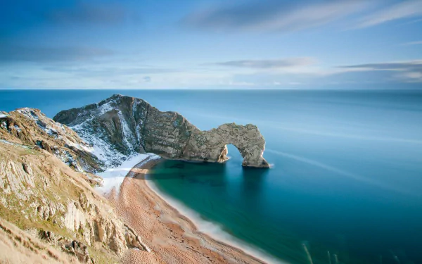 HD desktop wallpaper of Durdle Door, showcasing coastal cliffs and a natural rock arch over calm blue sea under a partly cloudy sky.