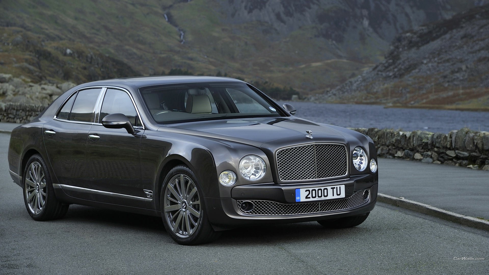HD PC desktop wallpaper of a 2013 Bentley Mulsanne vehicle parked by a lakeside road with rugged mountains in the background.